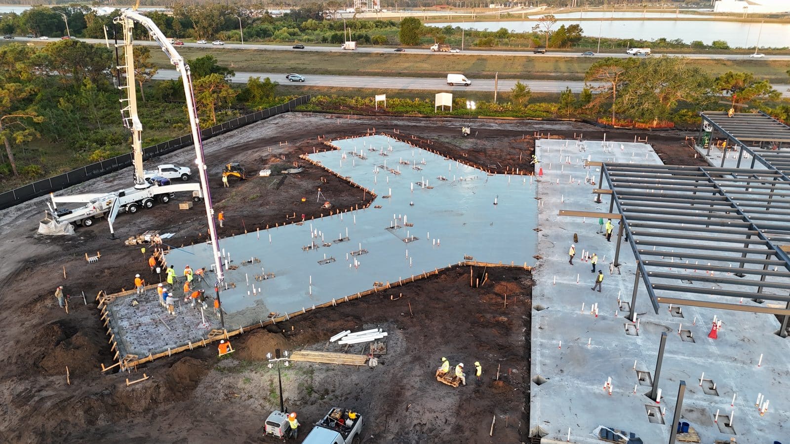 Concrete pump truck placing a commercial building slab beside the steel structure