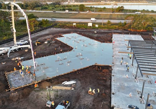 Concrete pump truck placing a commercial building slab beside the steel structure